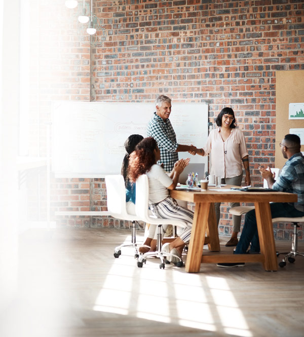 group of professionals in a modern office engaged in a meeting while one person shakes hands with another celebrating success and collaboration in a creative environment