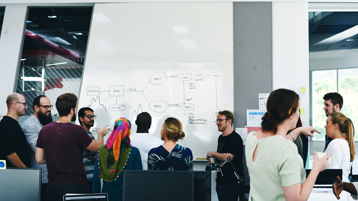 group of diverse professionals collaborating and discussing ideas around a whiteboard with diagrams and notes highlighting workflow and process improvement