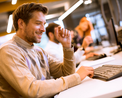 man smiling while typing on keyboard in modern office with two people in background